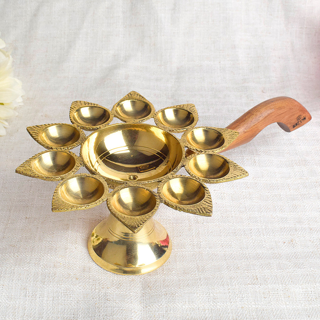 Dasmukhi Aarti Diya with Wooden Handle – A traditional brass oil lamp with a wooden handle, designed with ten wicks to enhance the spiritual experience during aarti rituals, creating a bright and holy ambiance for your prayers. India’s Largest Pooja Accessories Brand – www.satvikworld.com