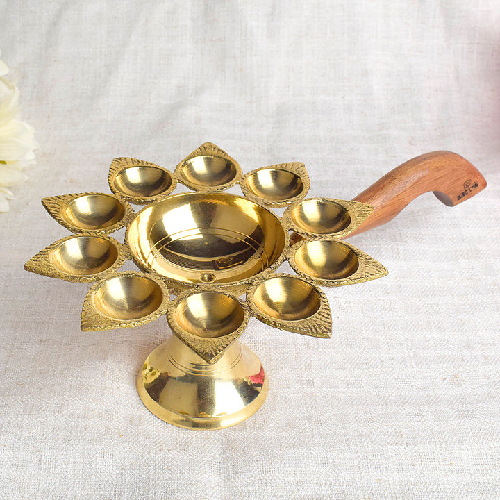 Dasmukhi Aarti Diya with Wooden Handle – A traditional brass oil lamp with a wooden handle, designed with ten wicks to enhance the spiritual experience during aarti rituals, creating a bright and holy ambiance for your prayers. India’s Largest Pooja Accessories Brand – www.satvikworld.com