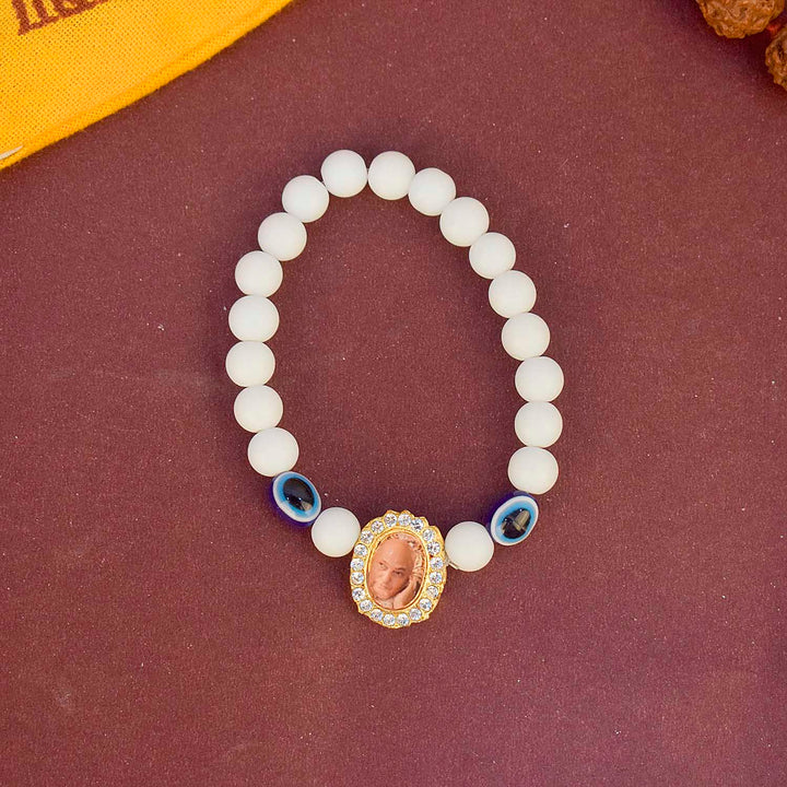White Beads with Evil Eye Single Layer Guruji Swaroop Bracelet featuring pure white beads accented with a blue evil eye bead and Jai Guruji Swaroop – perfect for spiritual wear, protection, and gifting. India’s Largest Pooja Accessories Brand – www.satvikworld.com