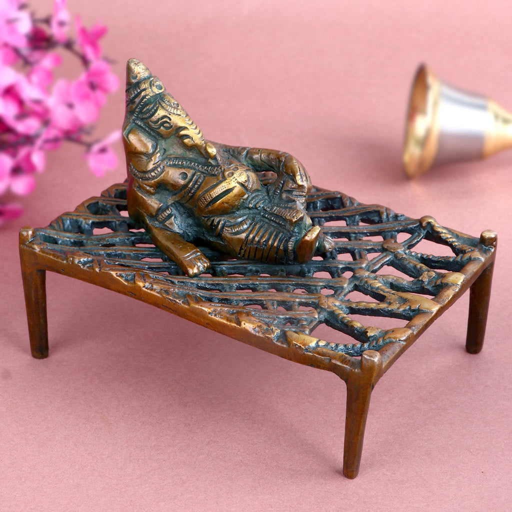 Antique brass Ganesha idol depicting Lord Ganesha relaxing on a traditional charpoy, intricately detailed to symbolize tranquility, wisdom, and divine blessings. Perfect for spiritual décor or worship. India’s Largest Pooja Accessories Brand – www.satvikworld.com